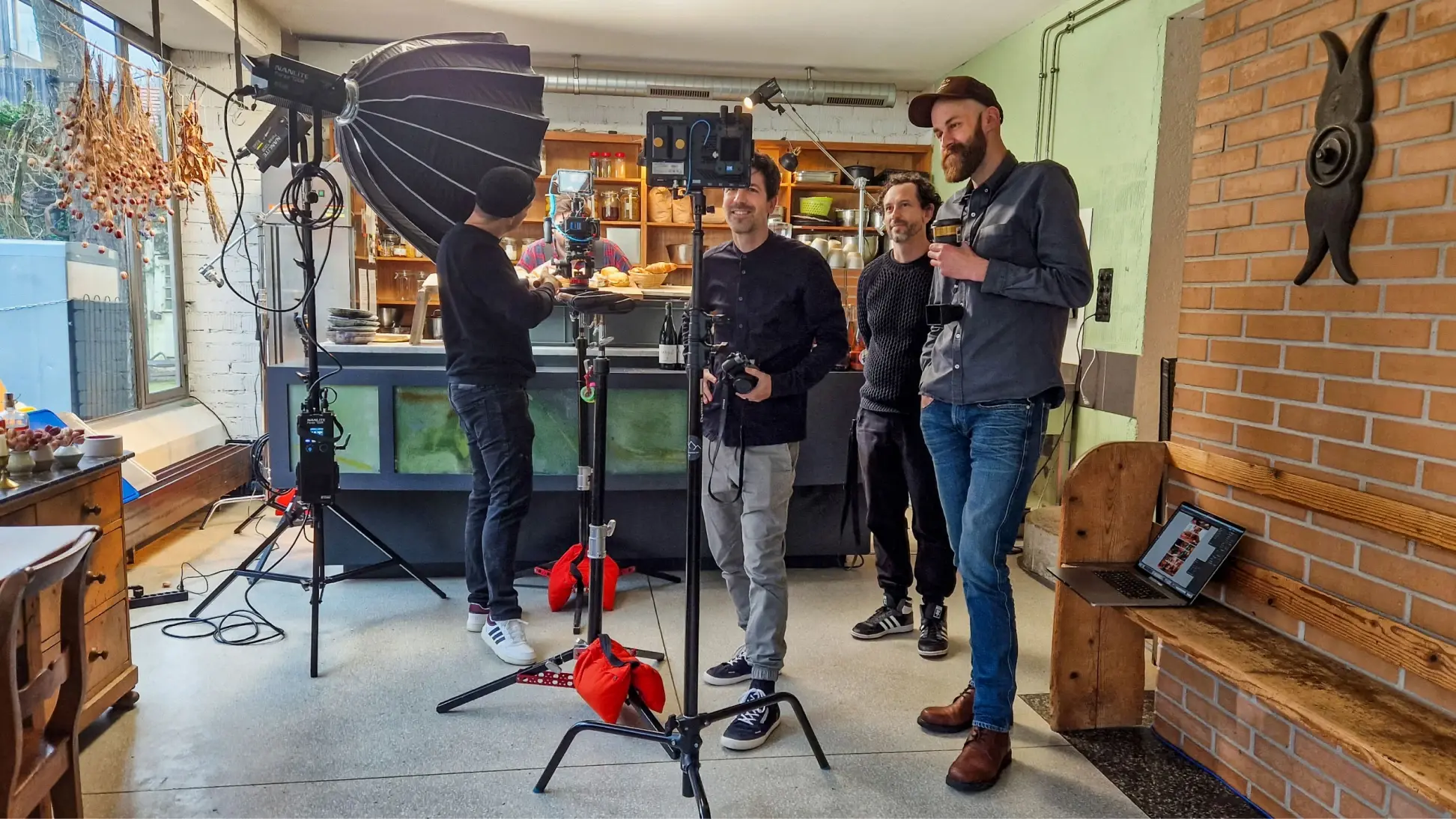 Vier Personen stehen in einem küchenähnlichen Studio mit professioneller Kamera- und Beleuchtungsausrüstung und bereiten sich darauf vor, Inhalte für eine nationale Kampagne für Schweizer Brot zu drehen. Ein Laptop liegt aufgeklappt auf einer Bank in der Nähe, während sie sich austauschen und einrichten.