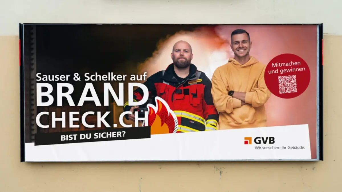Plakat mit zwei Männern, einer in Feuerwehruniform und einer im braunen Kapuzenpulli, werben für "BRANDCHECK.CH" mit dem Text "Bist du sicher?" und einem QR-Code für ein Gewinnspiel. Das Logo der GVB-Versicherung befindet sich unten rechts.